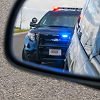 Police cruiser with flashing lights seen in rear view mirror after bing pulled over